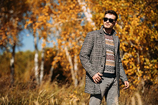 Un jeune homme portant des lunettes de soleil et un petit manteau à carreaux se promène dans la forêt automnale.