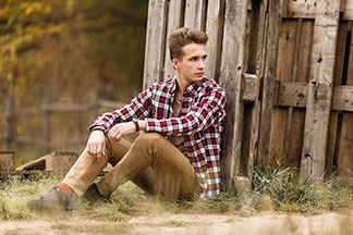 Un jour d'automne, un jeune homme en chemise manches longues à carreaux est assis dans un pré, appuyé sur une palette en bois.