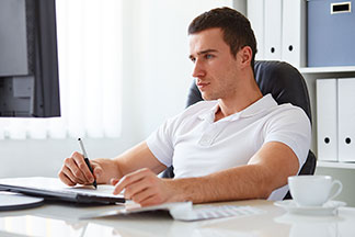 Convient également pour le bureau : un jeune homme en polo blanc est assis à son bureau devant son ordinateur.