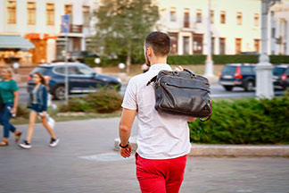 Un jeune homme en pantalon rouge et chemise blanche manches courtes traverse la ville avec sa serviette en cuir.