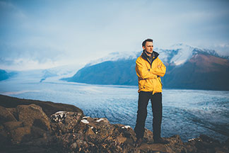 Équipés pour tous les défis : un jeune homme vêtu d'une veste jaune de sport d'hiver se tient devant un glacier.