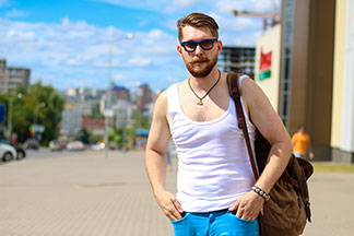 Un jeune homme portant un sous-vêtement hommes blanc, des lunettes de soleil et un sac à dos se promène tranquillement dans une ville.