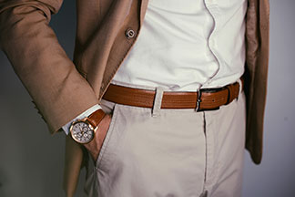 Combinez correctement les accessoires : gros plan d'un homme portant une montre avec un bracelet en cuir marron, une ceinture de couleur assortie et une veste assortie.