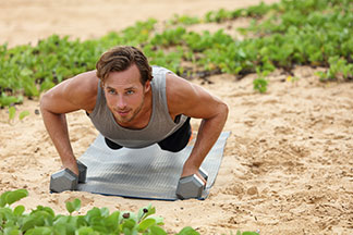 Un jeune homme avec un corps bien entraîné en t-shirt de sport sans manches fait ses exercices de fitness sur une plage.