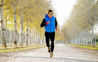 Un jeune homme sportif portant des lunettes de soleil et un gilet homme fait du jogging à travers un paysage automnal.