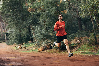 Un jeune homme sportif portant un t-shirt orange fonctionnel manches longues fait son jogging dans un parc.
