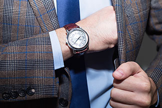 Les montres hommes attirent l'attention : gros plan sur une montre analogique au bras d'un homme portant une chemise bleu clair et une veste à carreaux.