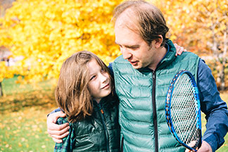 Des gilets hommes pour les petits et les grands : père et fils se tenant bras dessus bras dessous avec une raquette de tennis à la main dans la nature.