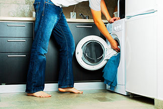 Un jeune homme est assis devant une machine à laver pour la mettre en marche. A côté de lui se trouve sa petite fille avec un panier à linge.