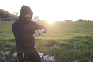 Des sweatshirts pour le sport : un homme portant un sweatshirt à capuche noir ainsi qu'un pantalon de jogging se tient dehors, la capuche relevée, et regarde sa montre.