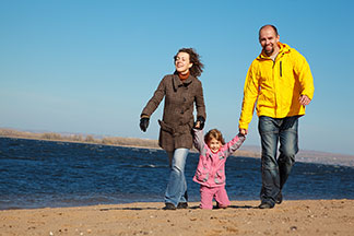 Un homme, une femme et leur jeune fille, tous vêtus avec des vestes mi-saisons, se promènent sur la plage un jour d'automne.