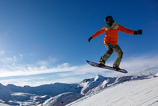 Vestes de sport hommes pour l'hiver : un snowboarder saute dans les montagnes enneigées.