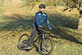 Un vététiste barbu portant un pantalon de jogging, une chemise, un casque et des lunettes de soleil fonctionnelles se tient debout par une journée ensoleillée sur une colline pour profiter de son tour.