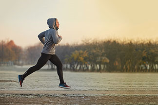 Un jeune homme fait son jogging dans un parc automnal au petit matin, vêtu d'une veste polaire grise avec une capuche.