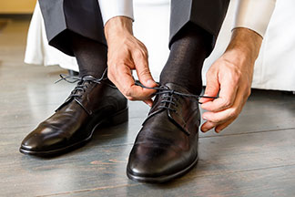Les bons bas hommes pour le bureau : gros plan d'un homme portant un pantalon de costume sombre et des bas marron foncé nouant les lacets de ses chaussures en cuir marron foncé.