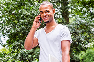 Un jeune homme portant un shirt blanche à col en V parle au téléphone dans un parc.